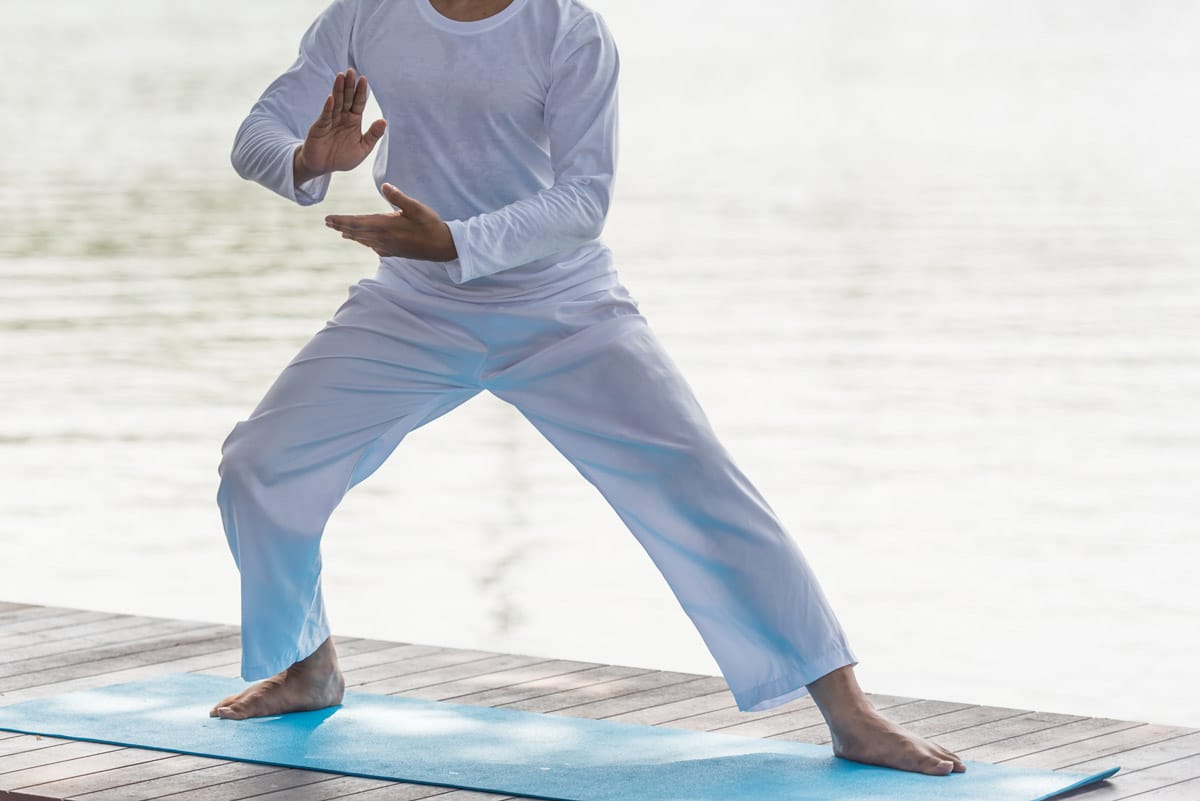 middle aged man dressed in white performing tai chi without the symptoms of cubital tunnel syndrome in his elbows