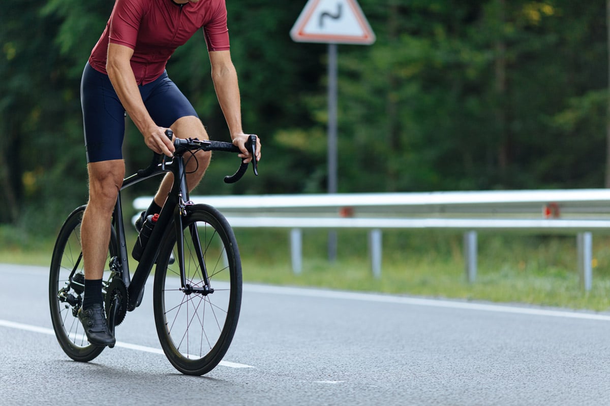 male cyclist wearing blue shorts and a red jersey riding a bicycle on road surrounded by bushland without clavicle reduction symptoms