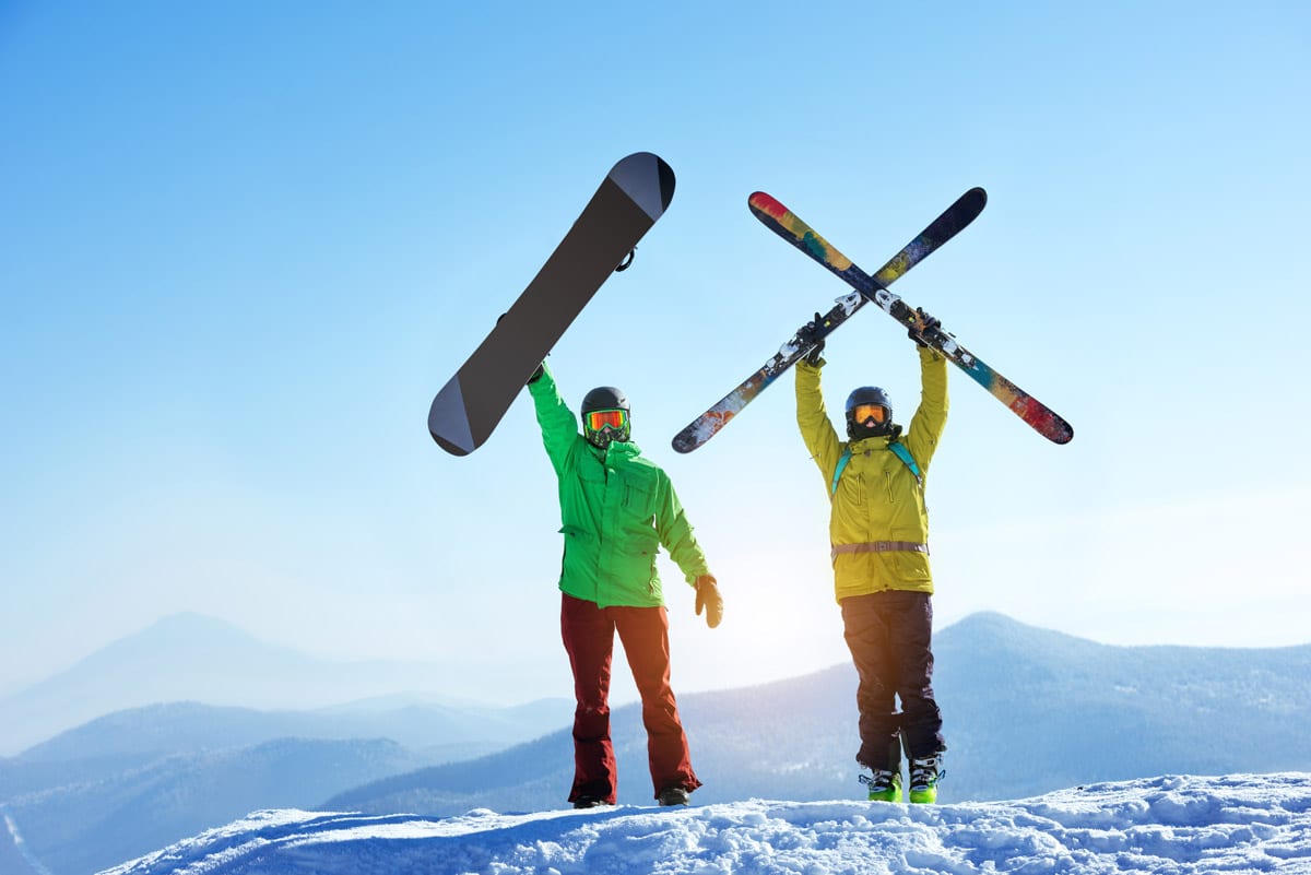 a skier and snowboarder dressed in bright green and yellow jackets standing on a snowy mountain top raising their snow equipment without symptoms of humerus clavicle elbow fractures